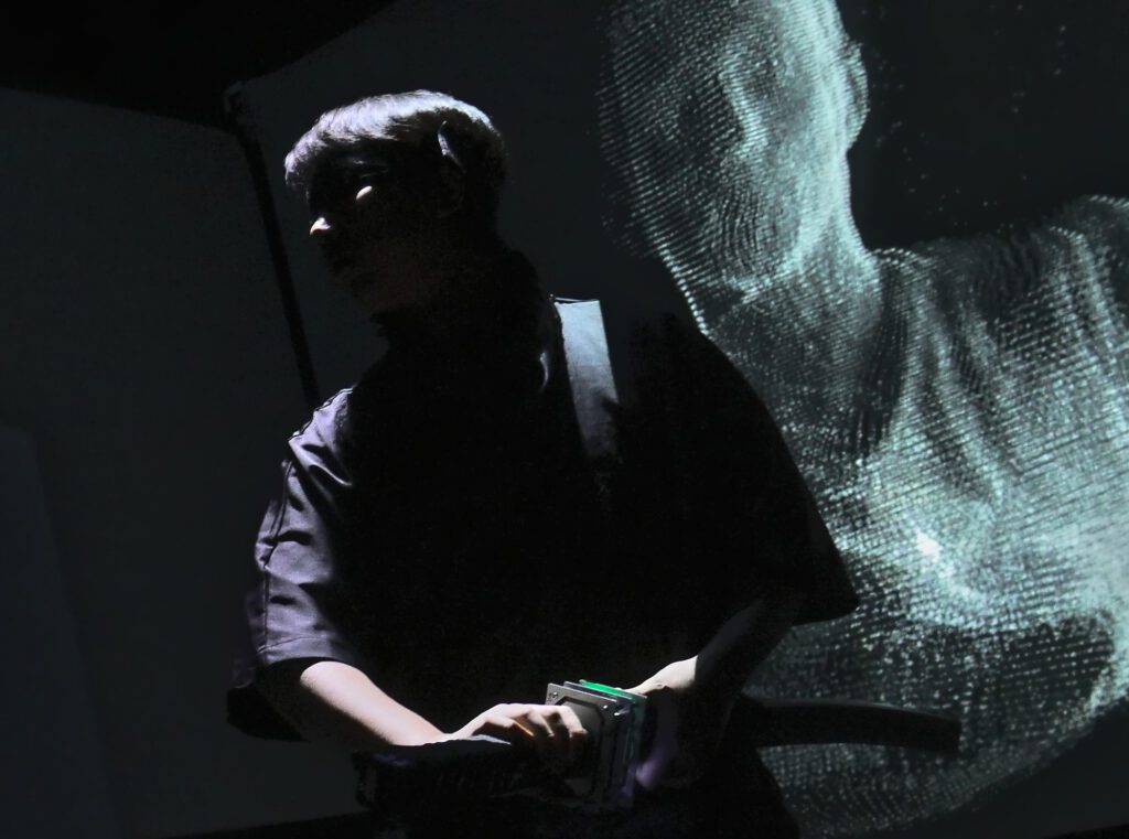 Eine Gestalt im Dunklen mit der Hand an einem Schwert. Im Hintergrund ein geisterhaftes Abbild der Gestalt aus weißen Pixeln.