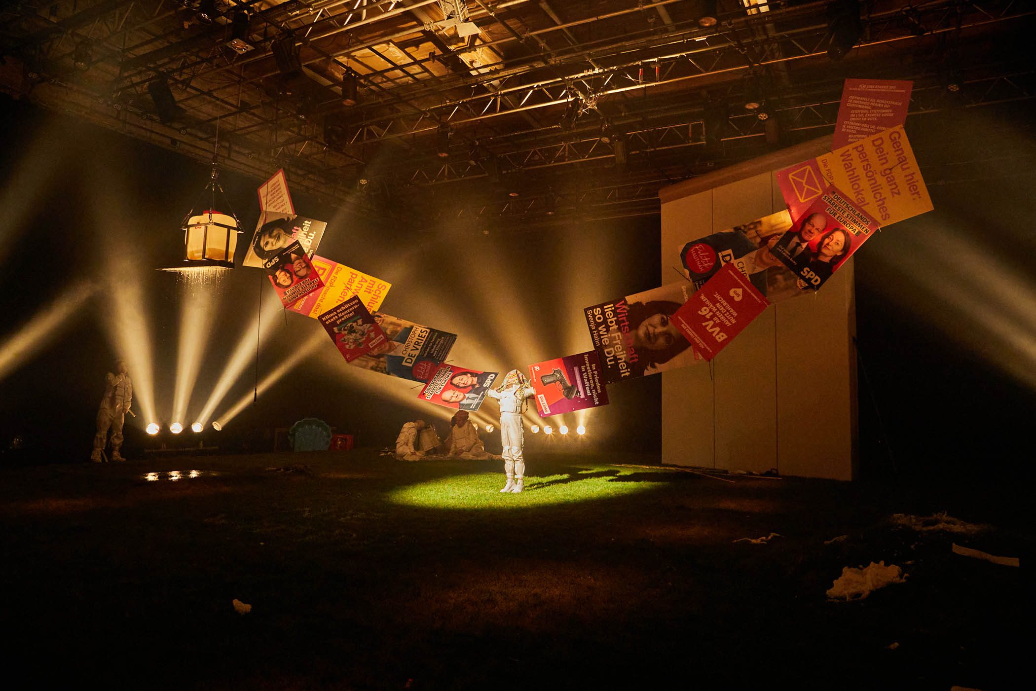 Performer_in einem Bühnenraum mit Papierflügeln und Scheinwerfern